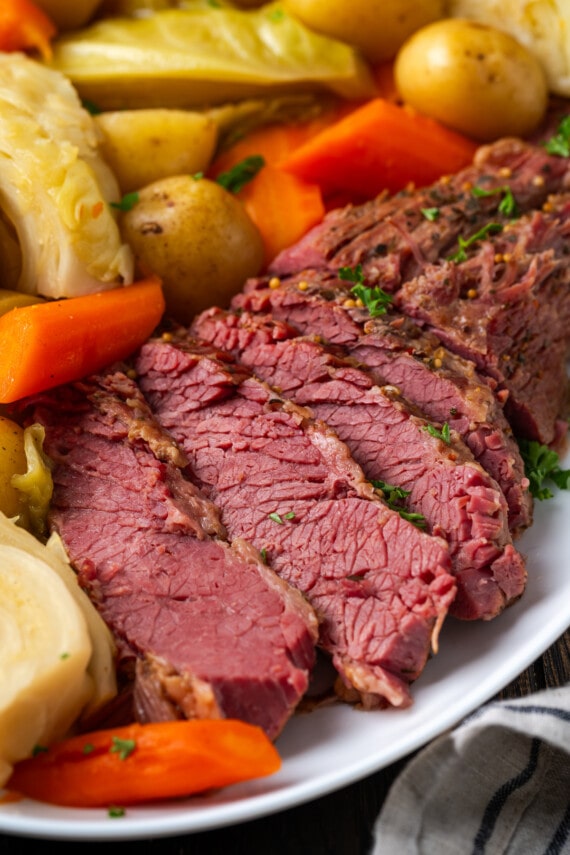In Scheiben geschnittenes Corned Beef auf einem Teller neben Kohl, Kartoffeln und Karotten.