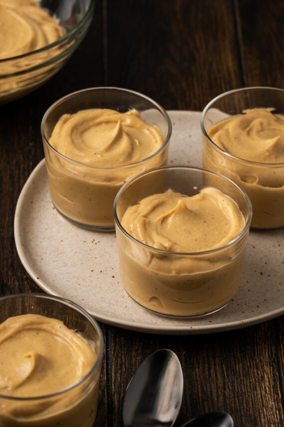 Bourbon-Butterscotch-Pudding wird in Gläsern auf einem Tablett serviert, neben weiteren Gläsern auf einem Tisch.