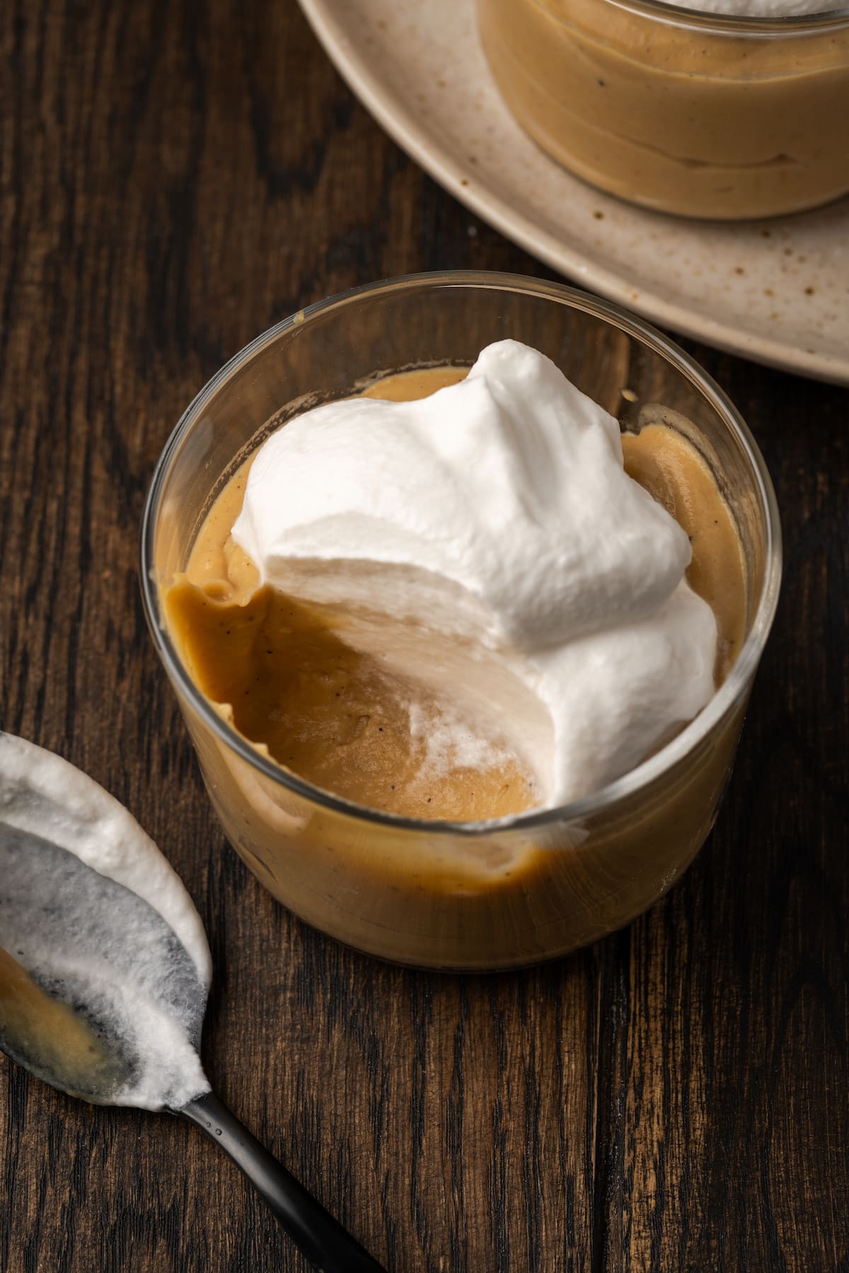 Buttertoffee-Pudding mit Schlagsahne in einem Glas, wobei ein Löffelchen fehlt.