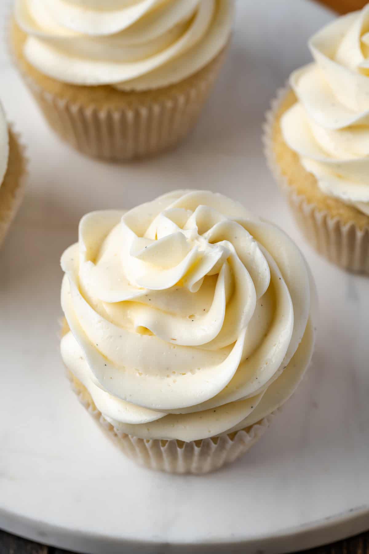 Nahaufnahme von Cupcakes mit Wirbeln aus Schweizer Baiser-Buttercreme auf einem Marmorkuchenständer.